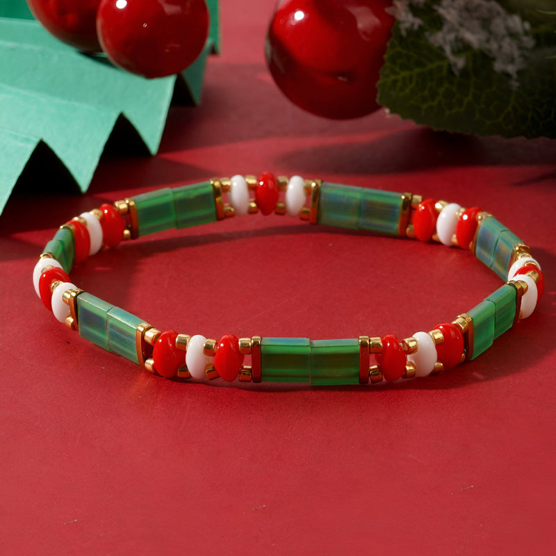 Bracelet féminin en perles vertes, blanches et rouges style Noël, modèle Santana sur fond rouge festif.