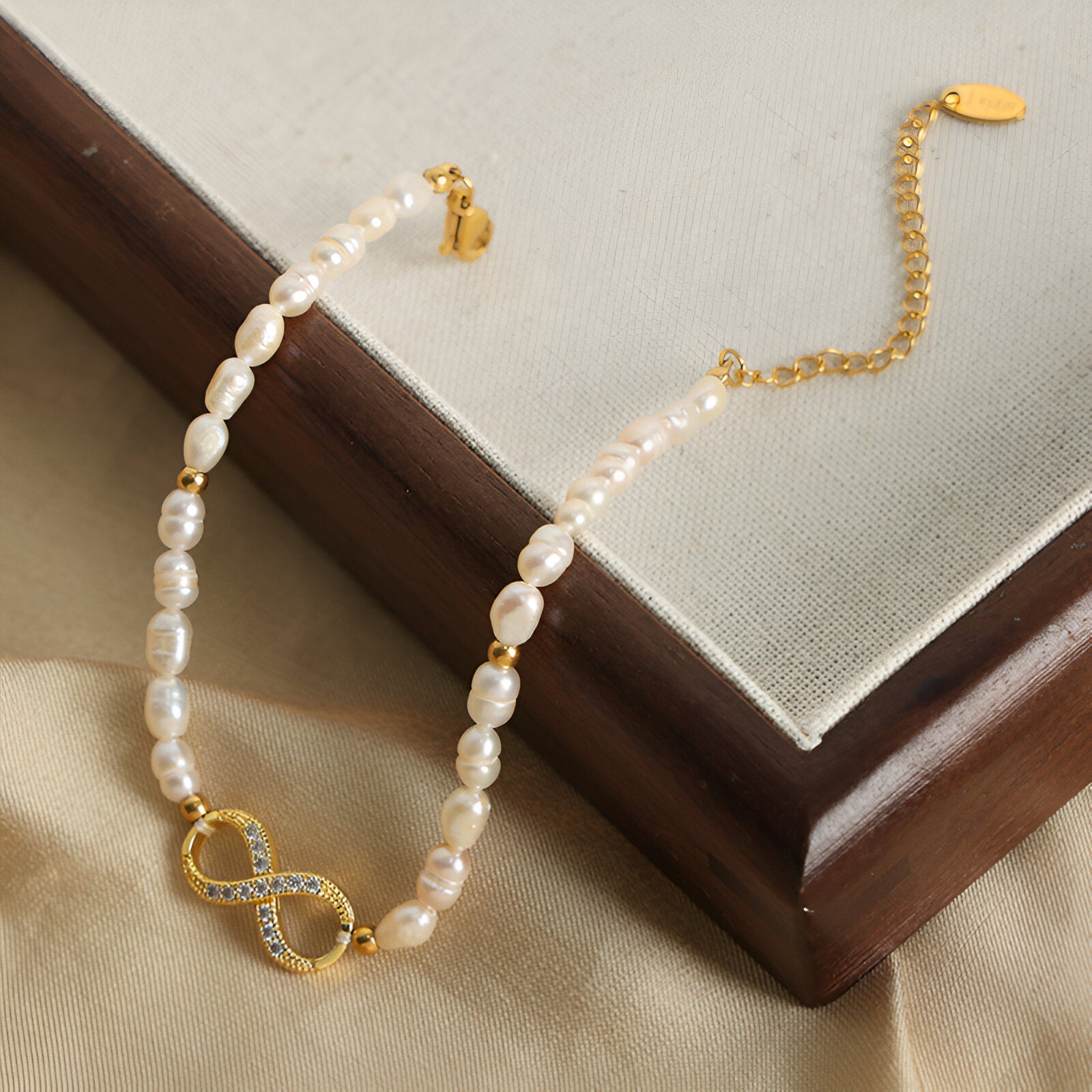Bracelet en perles naturelles blanches avec motif infini en or serti de zircones brillantes.