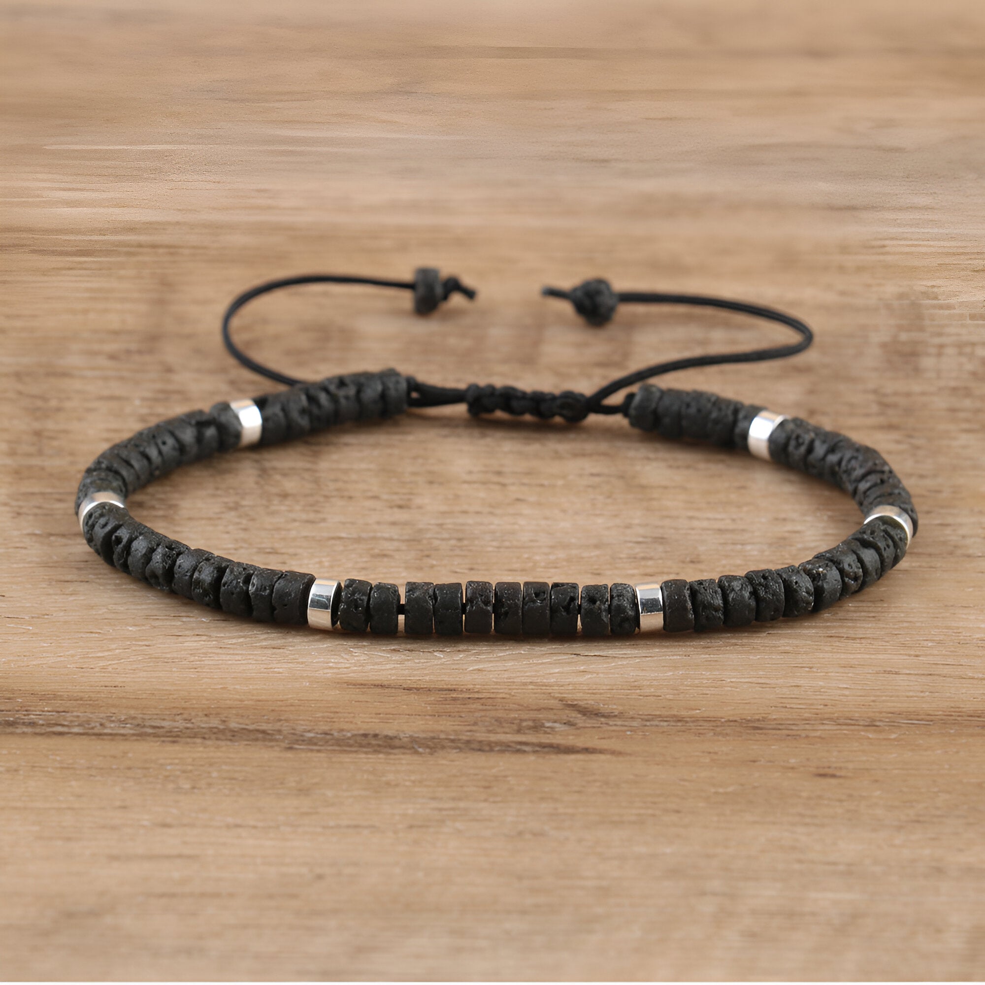 Bracelet mixte avec perles heishi noires en pierre volcanique et détails métalliques argentés, cordon réglable.