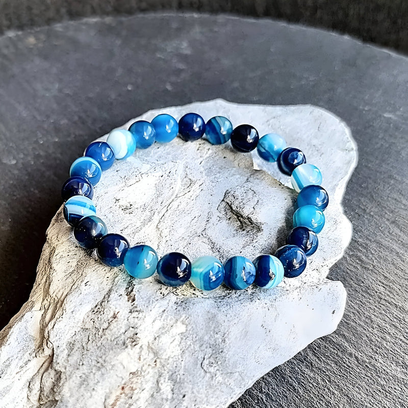 Bracelet mixte en pierre d'agate bleu à perles rondes sur fil élastique posé sur pierre grise.