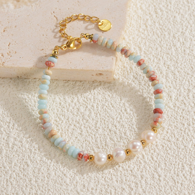 Bracelet or avec perles fines blanches, pierres naturelles bleu clair et touches rouges, fermoir chaîne réglable.