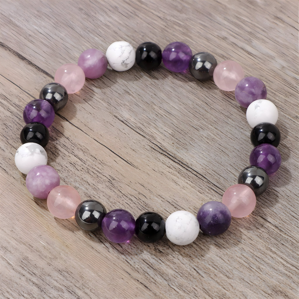Bracelet élastique à perles rondes en pierres naturelles violettes, blanches, noires et roses sur fond bois clair.