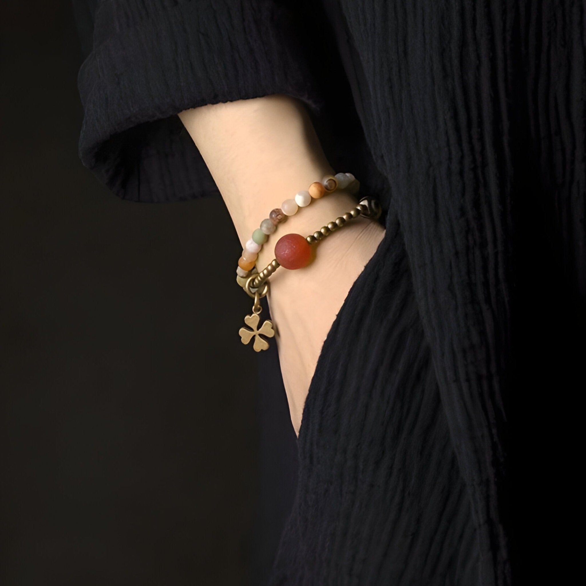 Bracelet femme en pierres naturelles d'agate jaune multicolore avec breloque trèfle dorée sur poignet.
