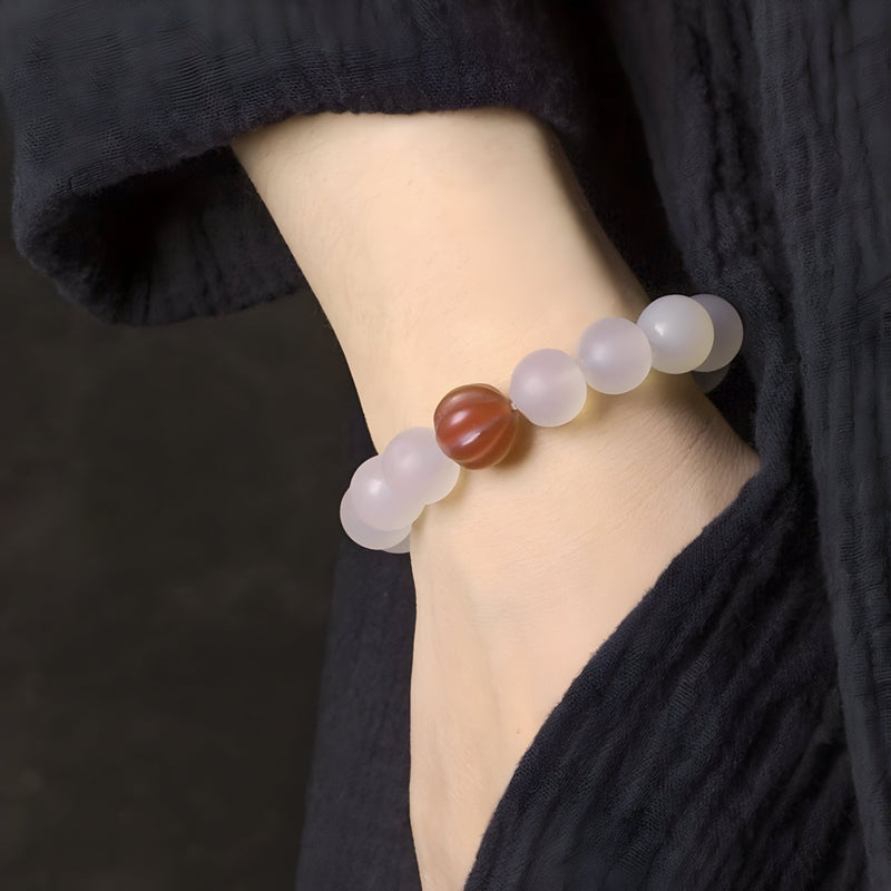Bracelet en agate naturelle avec perles translucides blanches et une perle centrale rouge rayée porté au poignet.