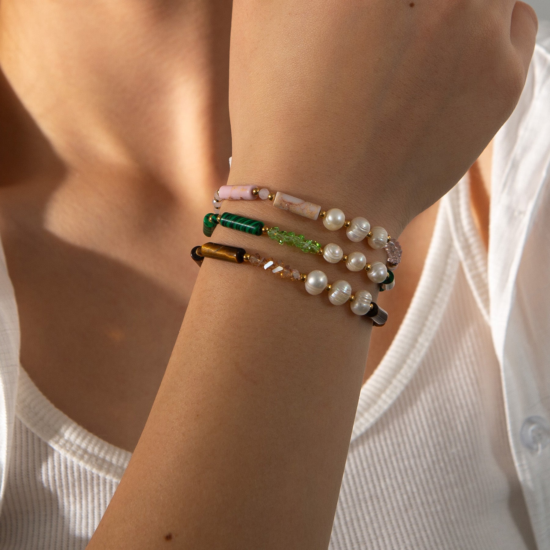 Bracelets empilés en perles naturelles vertes, roses, ocres avec rangées de perles blanches brillantes.