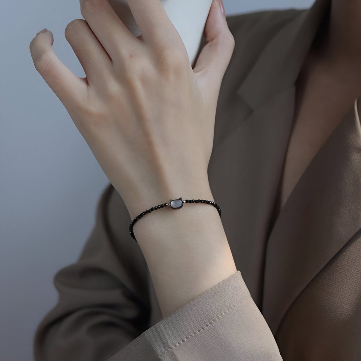 Bracelet fin avec perles noires et tête de chat en cristal blanc sur poignet féminin.