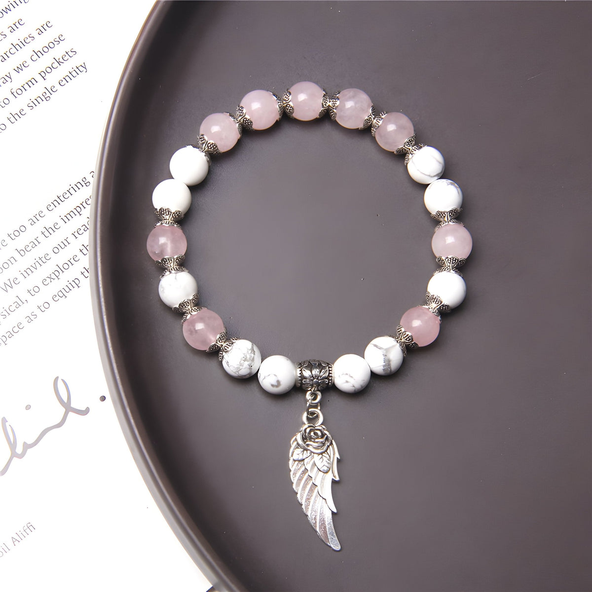 Bracelet mixte en pierres naturelles rose et blanches avec charme en forme de plume argentée.