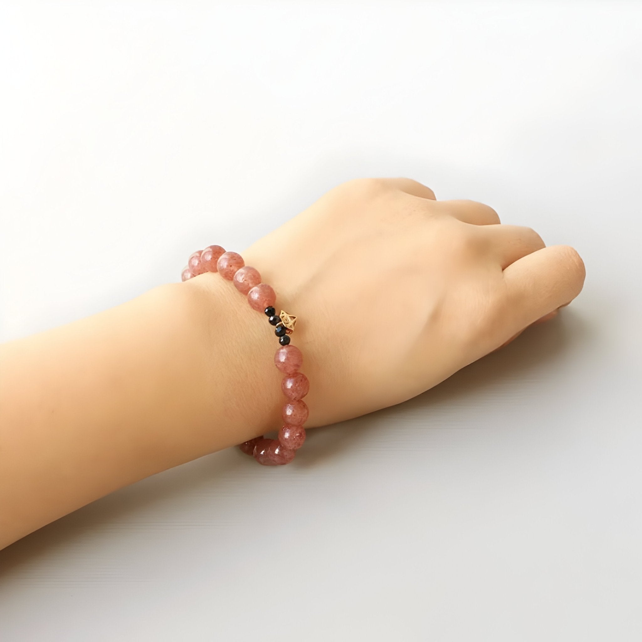 Bracelet en quartz rose avec perles rondes et petit détail doré, porté au poignet féminin.