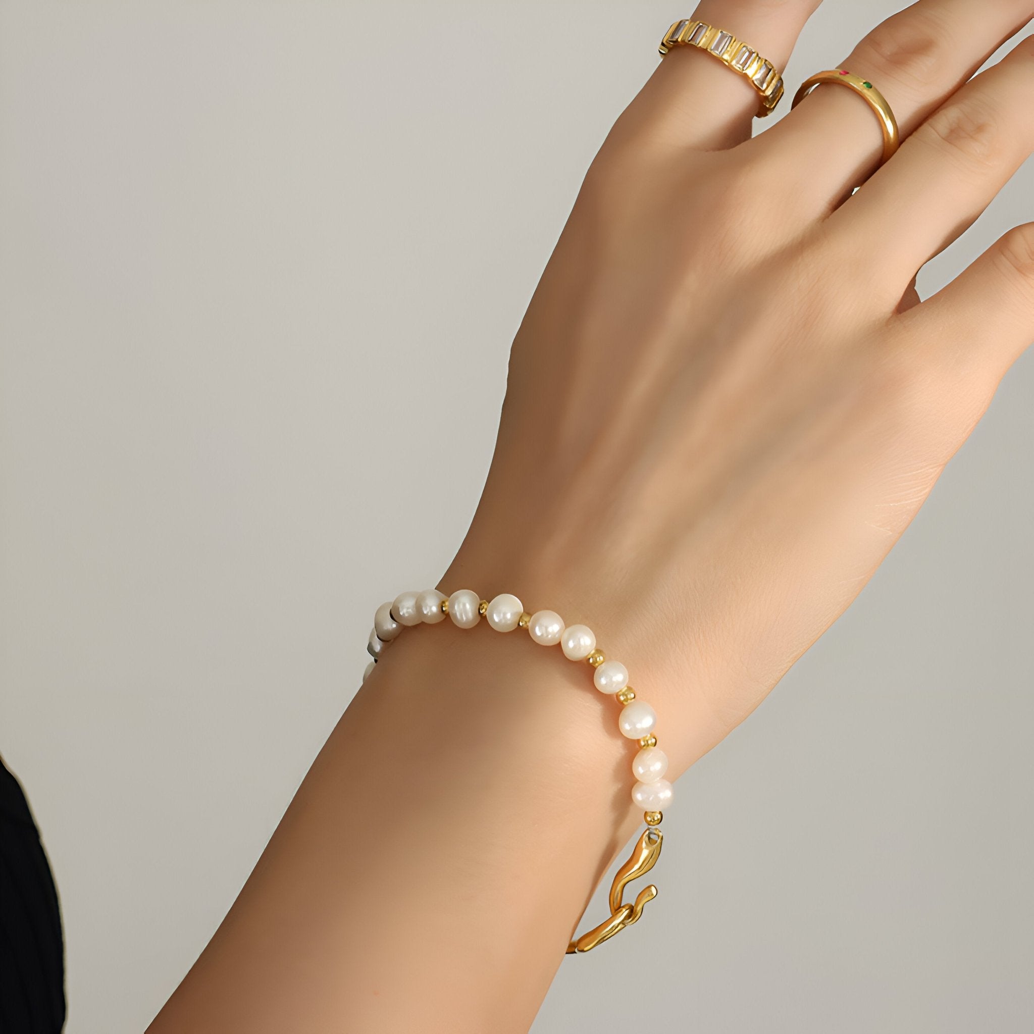 Bracelet en titane plaqué or 14 carats avec perles blanches rondes sur poignet féminin.