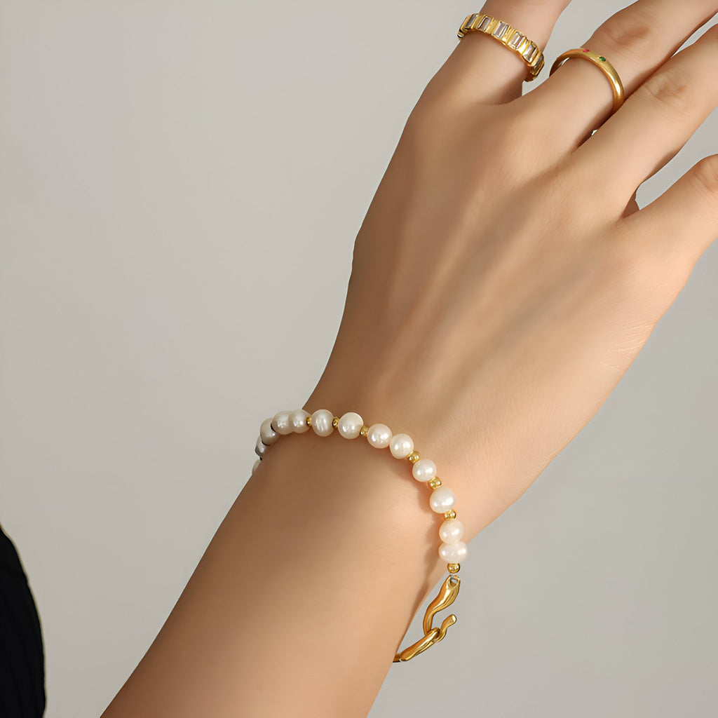 Bracelet en titane plaqué or 14 carats avec perles blanches rondes sur poignet féminin.