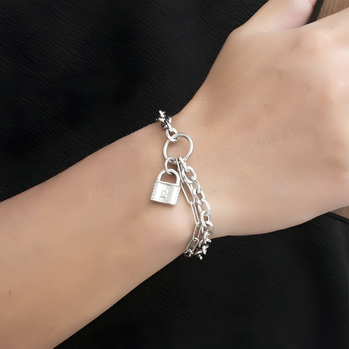 Bracelet en titane argenté maille forçat avec charm cadenas, porté au poignet, style mixte.