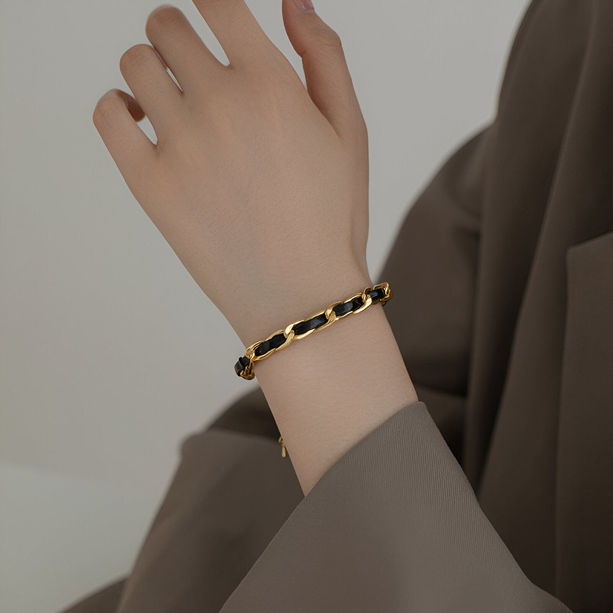 Bracelet en titane plaqué or avec chaîne noire et cordelette en cuir sur poignet féminin.