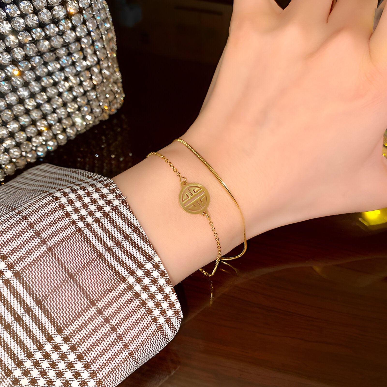 Bracelet fin en titane plaqué or 18 carats avec médaillon rond à motif géométrique porté au poignet féminin.