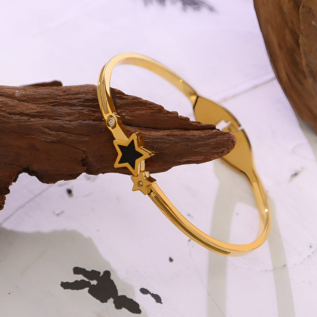 Bracelet jonc en titane plaqué or 18 carats avec étoile noire centrale et petits détails étoilés.