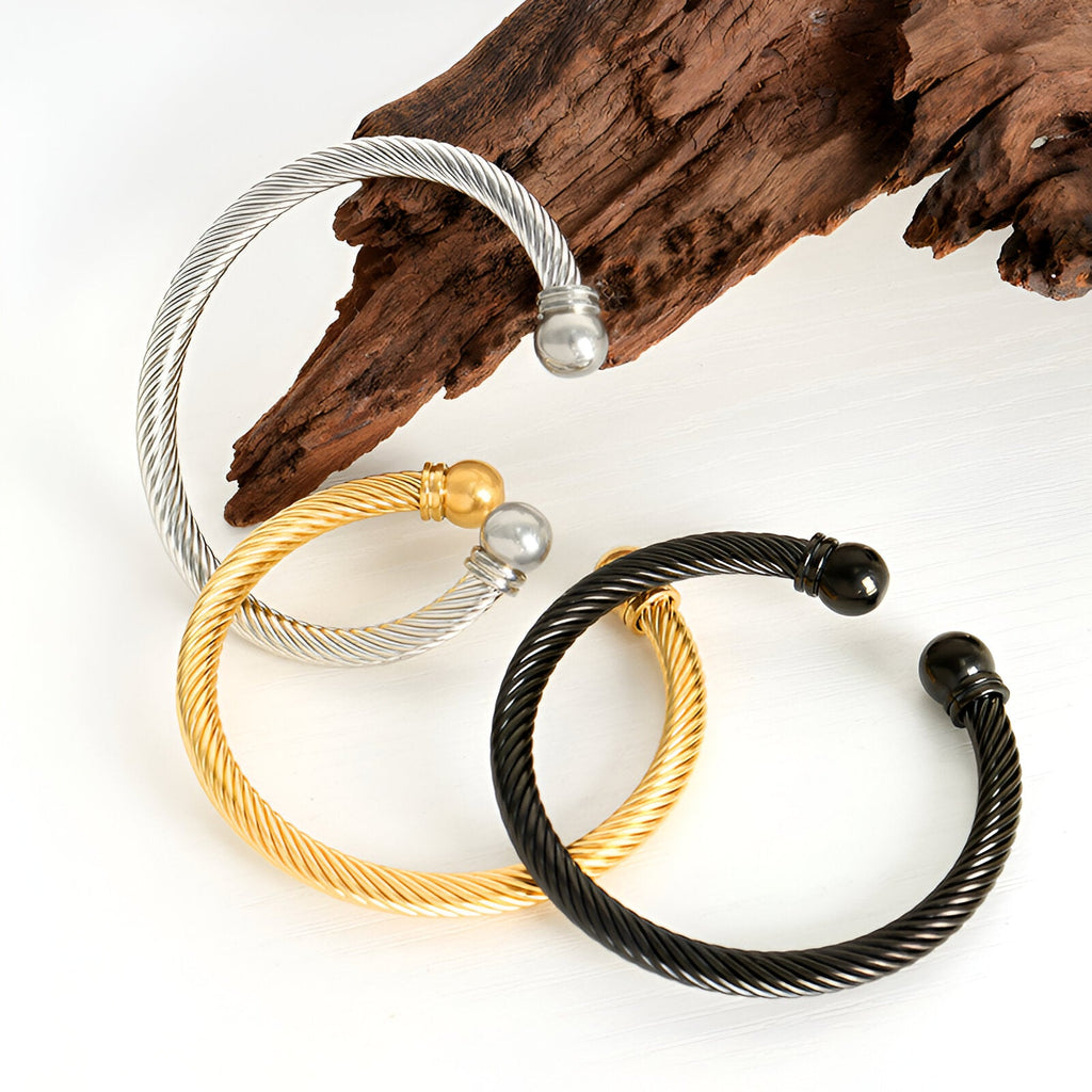 Trois bracelets torsadés ouverts en titane plaqué or, argent et noir, design simple et moderne.