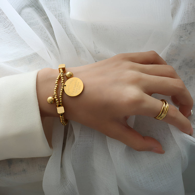 Bracelet en titane plaqué or avec perles dorées et médaillon rond porté au poignet.