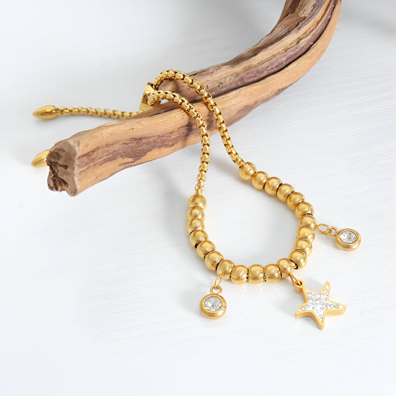 Bracelet en titane plaqué or à perles rondes et médaillon étoile serti de pierres blanches.