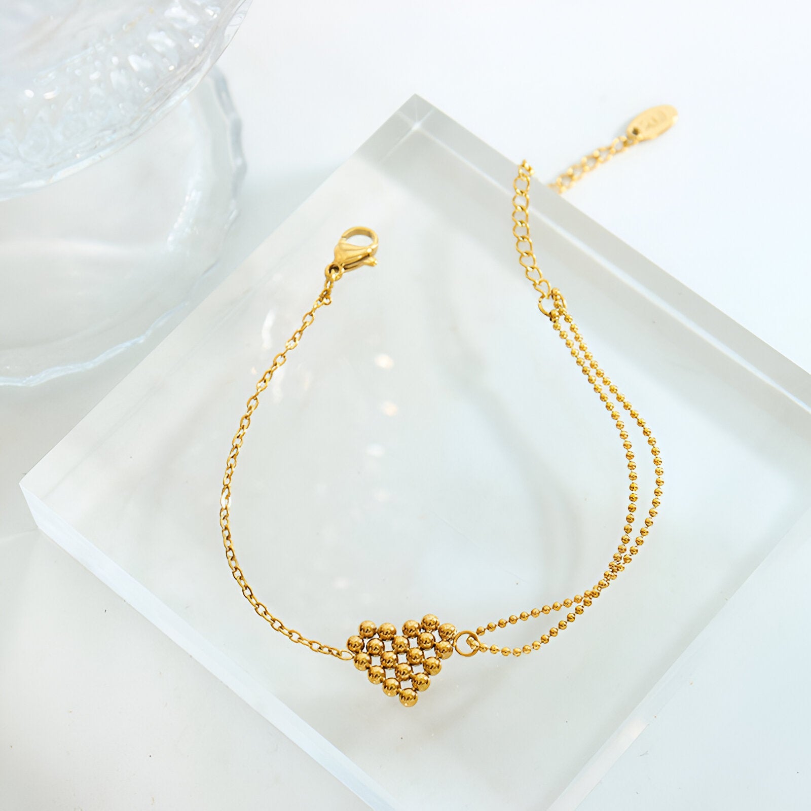 Bracelet fin en titane plaqué or avec motif cœur perlé et chaîne délicate.