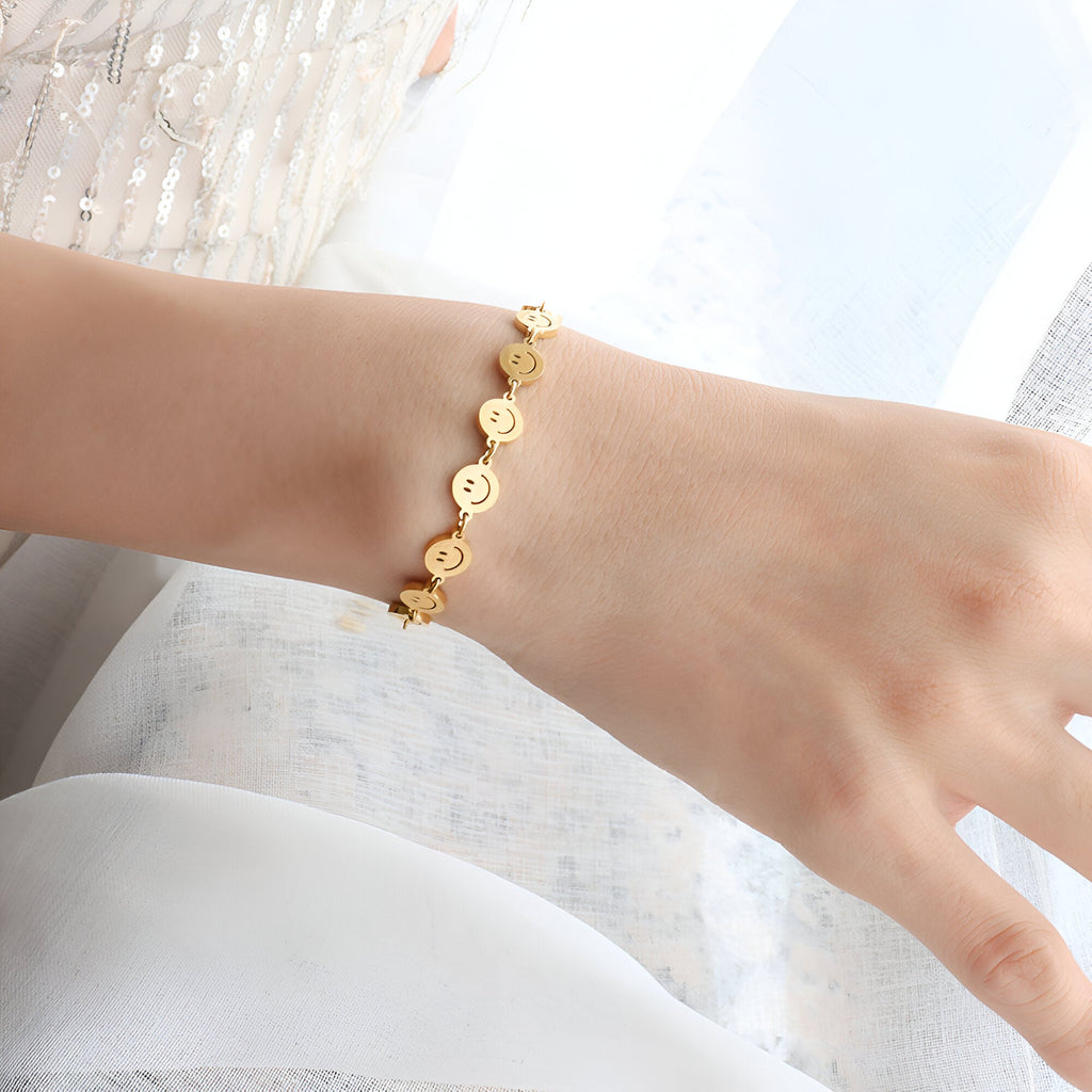 Bracelet fin en titane plaqué or avec motifs smileys alignés sur poignet féminin.