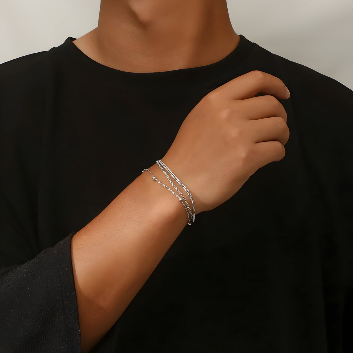 Bracelet triple en titane argenté fin et élégant porté au poignet d'un homme vêtue d'un haut noir.