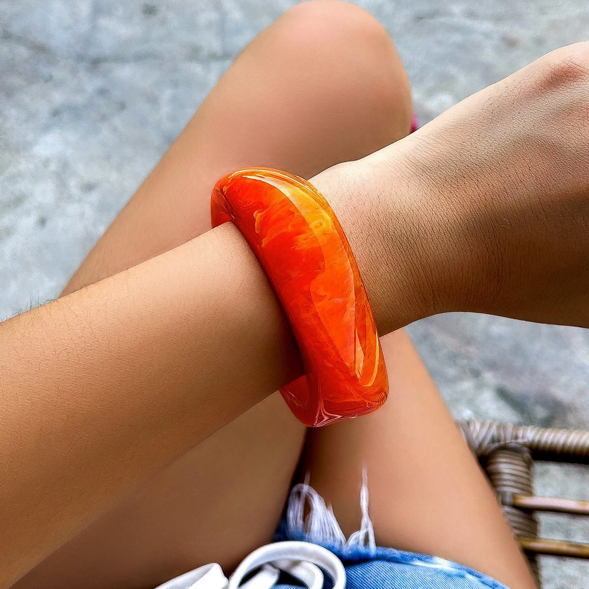 Bracelet épais en acrylique orange translucide au style moderne porté au poignet féminin.