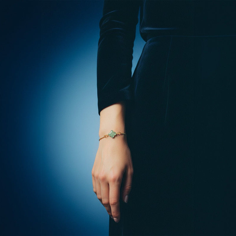 Bracelet fin à cordon noir avec pierre naturelle taillée en trèfle vert et fermoir coulissant doré.