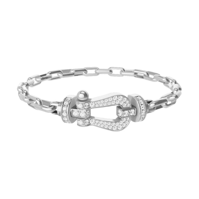 Bracelet femme en acier argenté avec chaîne forçat fine et fermoir fer à cheval serti de petits cristaux blancs.