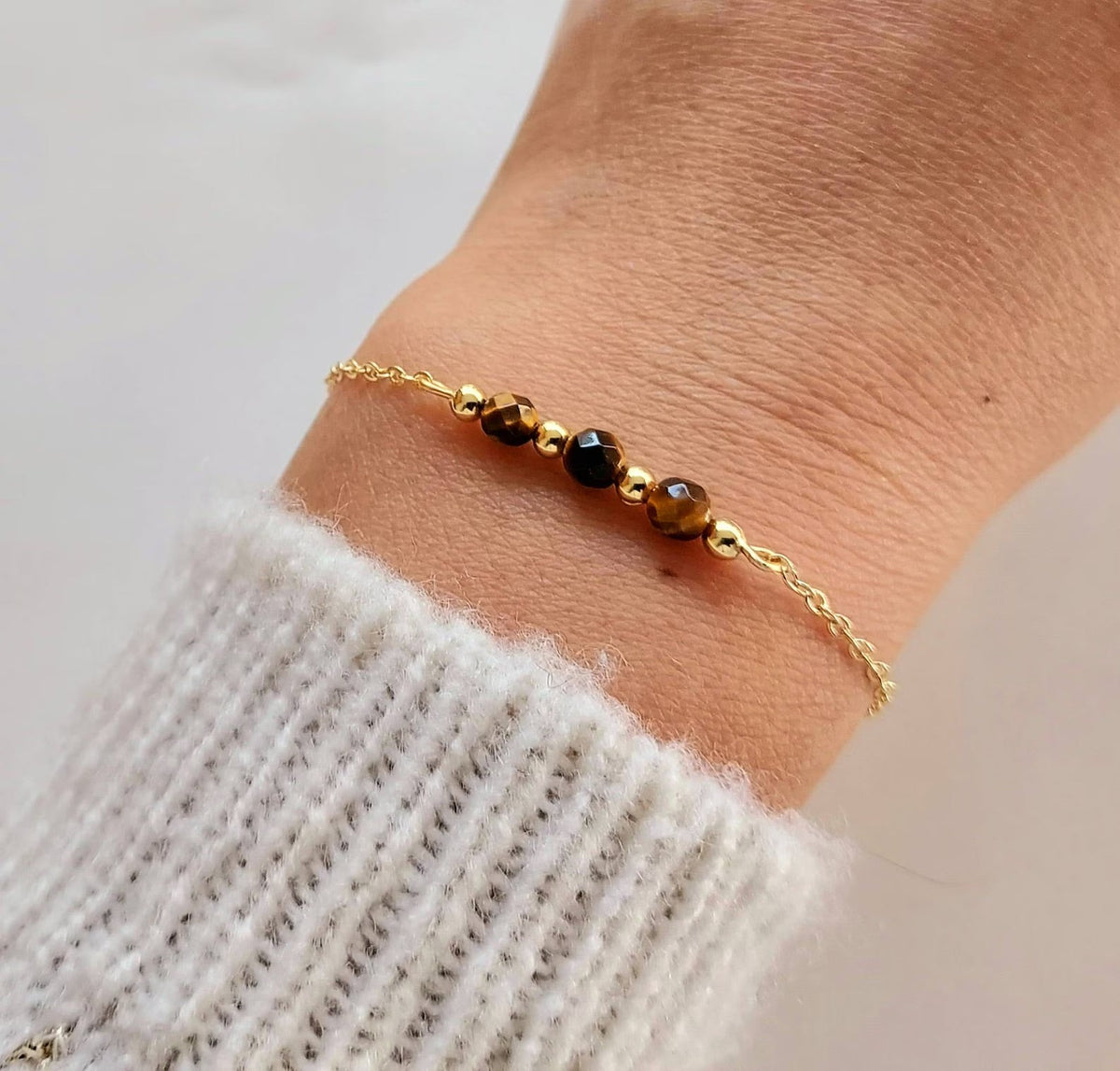 Bracelet fin en acier doré avec maille forçat et trois pierres semi-précieuses facettées noires et dorées.
