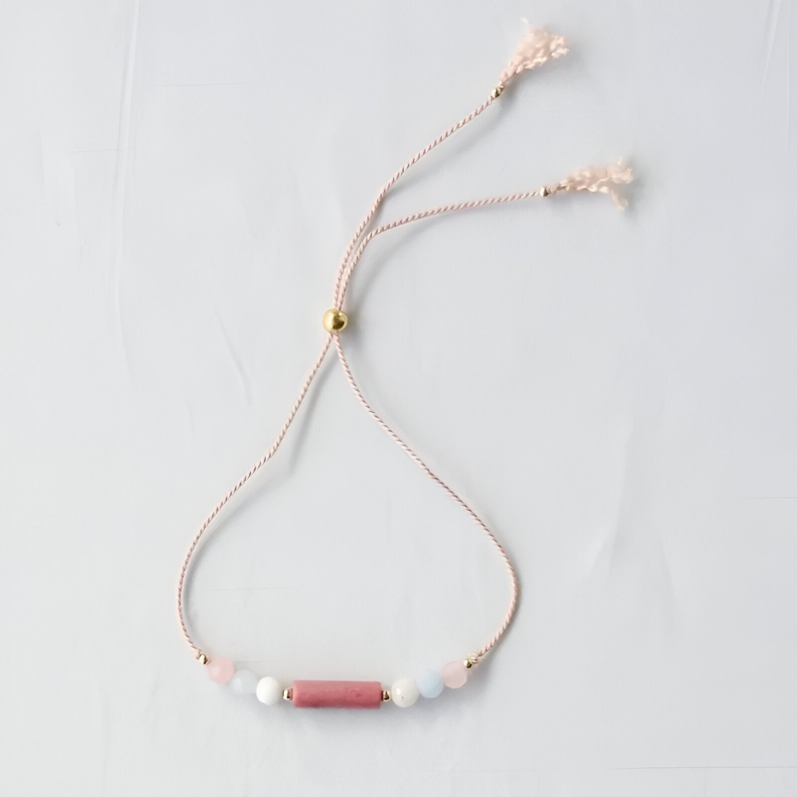 Bracelet fin réglable en cordon rose avec perles naturelles blanches, roses et dorées.