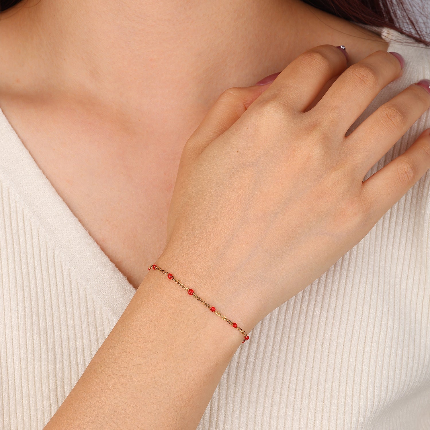 Bracelet fin doré en acier inoxydable avec perles rouges et fermeture mousqueton sur poignet féminin.