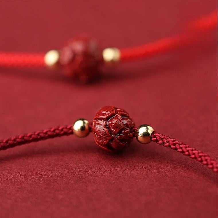 Bracelet en coton fil rouge avec perle cinabre rouge gravée d’une fleur de lotus et petites perles dorées.