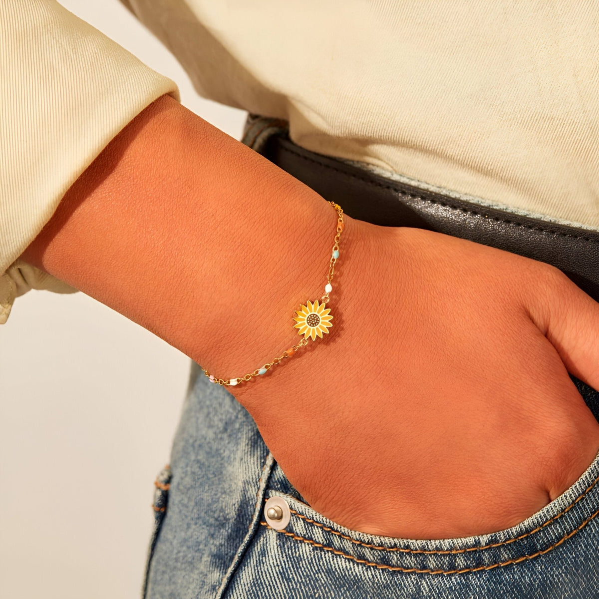 Bracelet fin en or avec pendentif fleur délicate porté au poignet féminin.