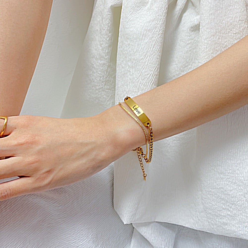 Bracelet gourmette en acier inoxydable doré, ajustable, avec plaque fine et chaînette sur poignet féminin.