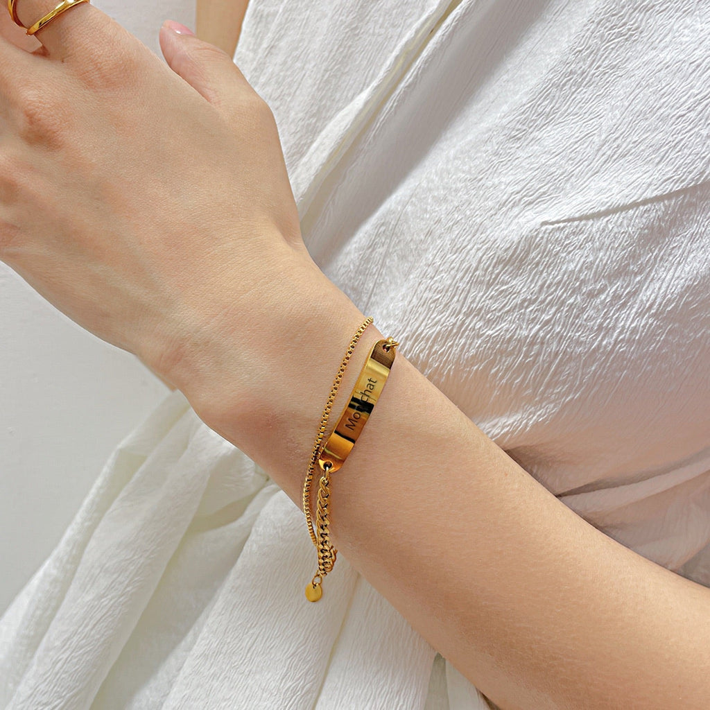 Bracelet gourmette ajustable en acier inoxydable doré avec plaque personnalisable porté au poignet féminin.