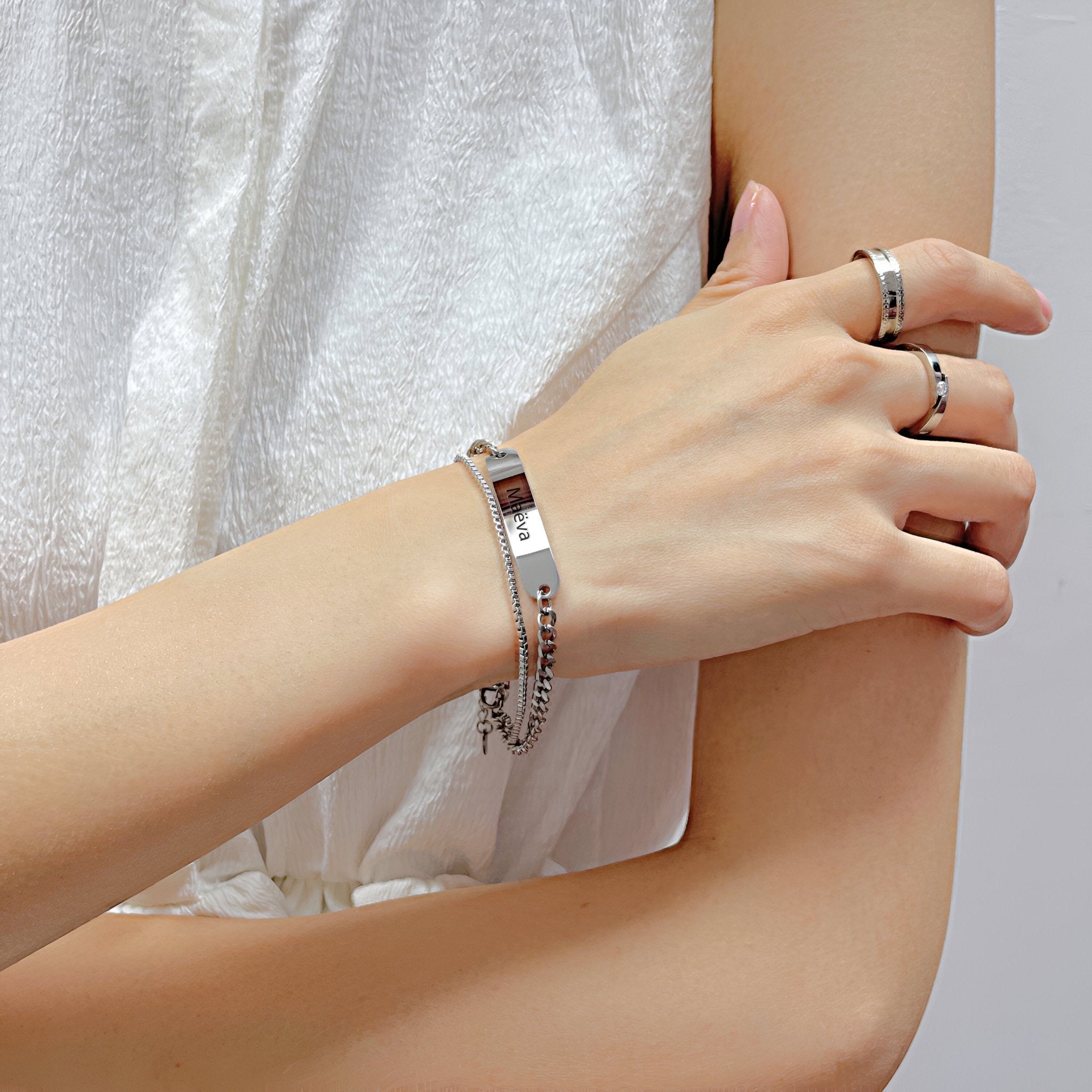 Bracelet gourmette en acier inoxydable argenté avec plaque personnalisable porté sur un poignet féminin, style ajustable.