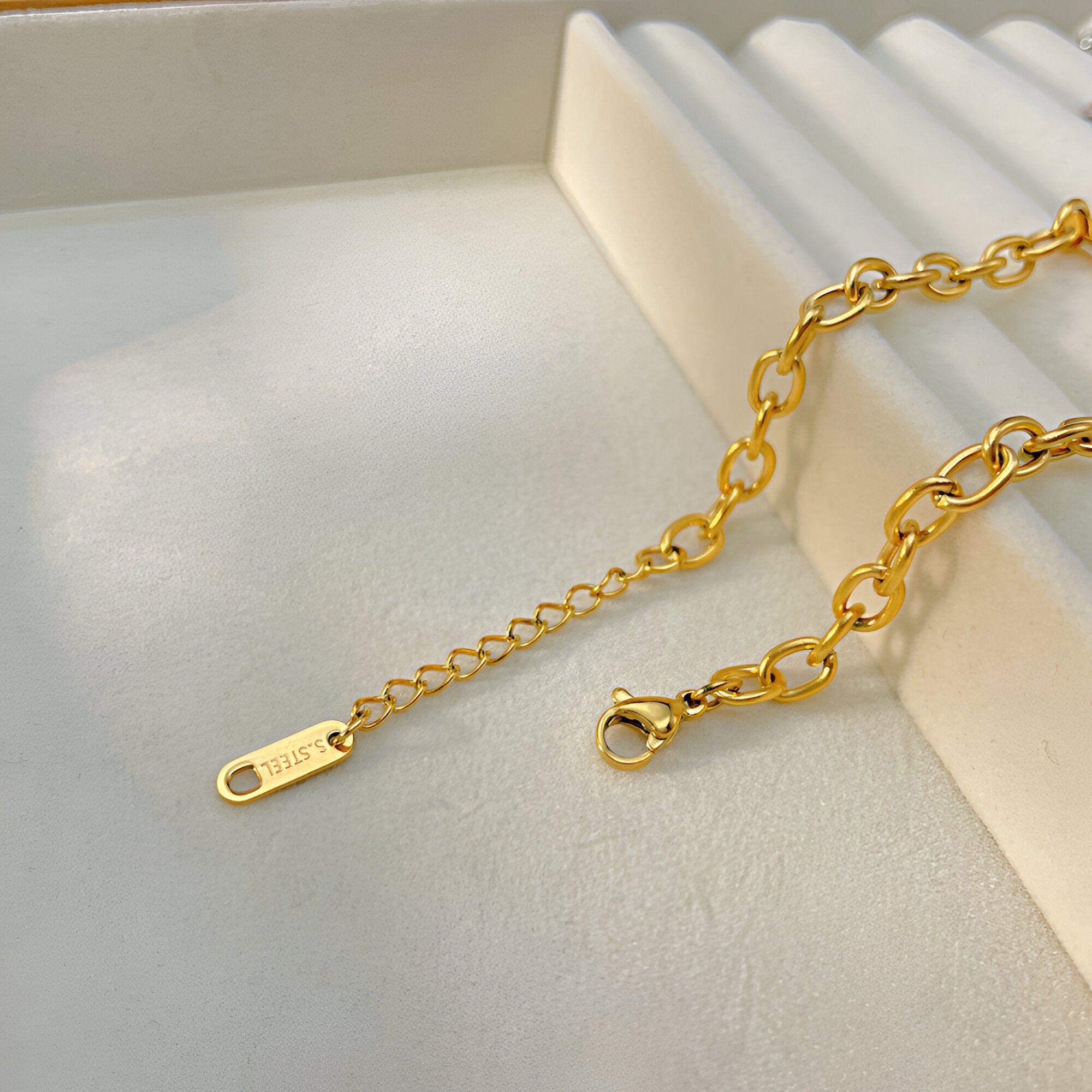 Bracelet gourmette doré en acier inoxydable avec chaîne fine et maillons ovales, fermoir mousqueton, détail pendentif gravé.