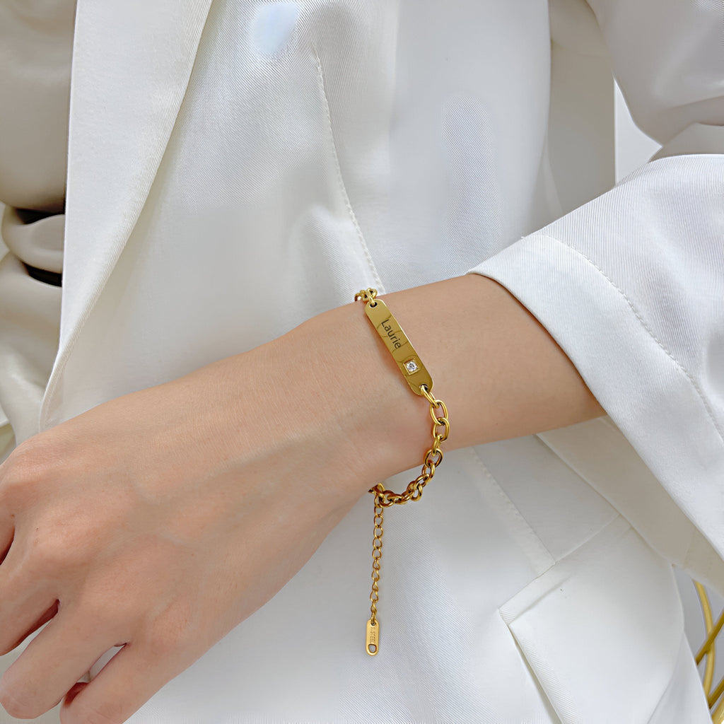 Bracelet gourmette en acier inoxydable doré avec plaque personnalisée et pierre zirconium, porté au poignet féminin.
