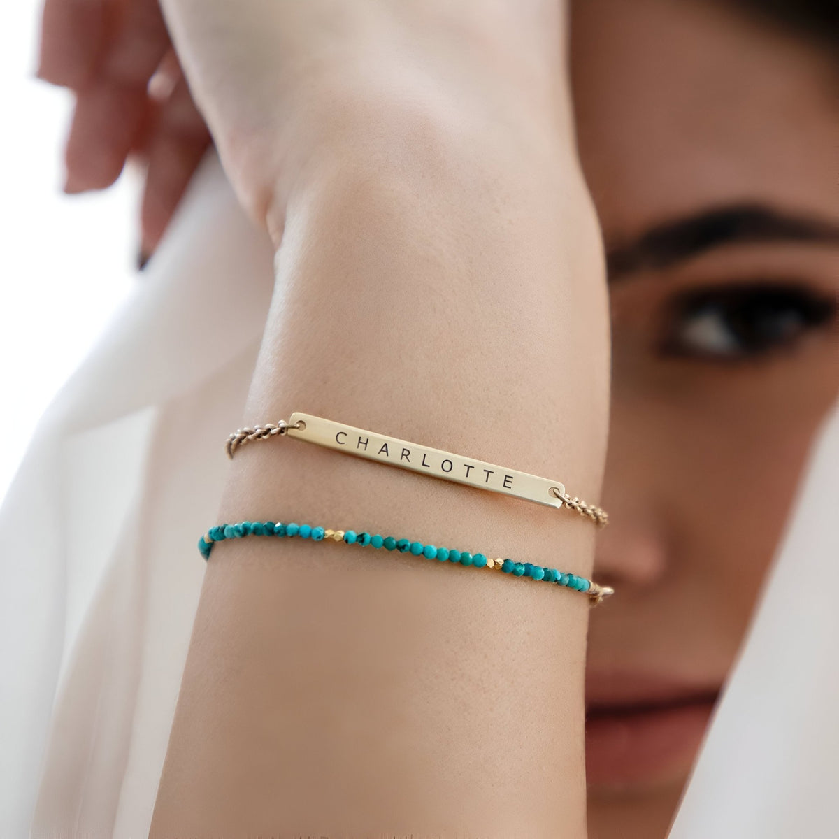 Bracelet gourmette en acier inoxydable doré avec gravure "CHARLOTTE" et bracelet perles turquoise porté au poignet féminin.