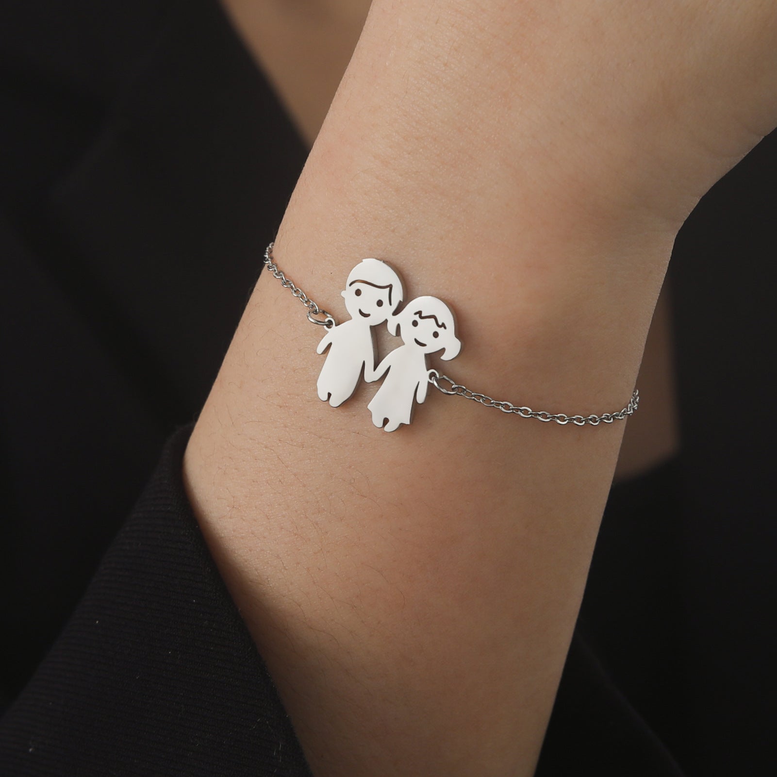 Bracelet fin en acier inoxydable argenté avec pendentif garçon et fille stylisés, design minimaliste et chaîne délicate.