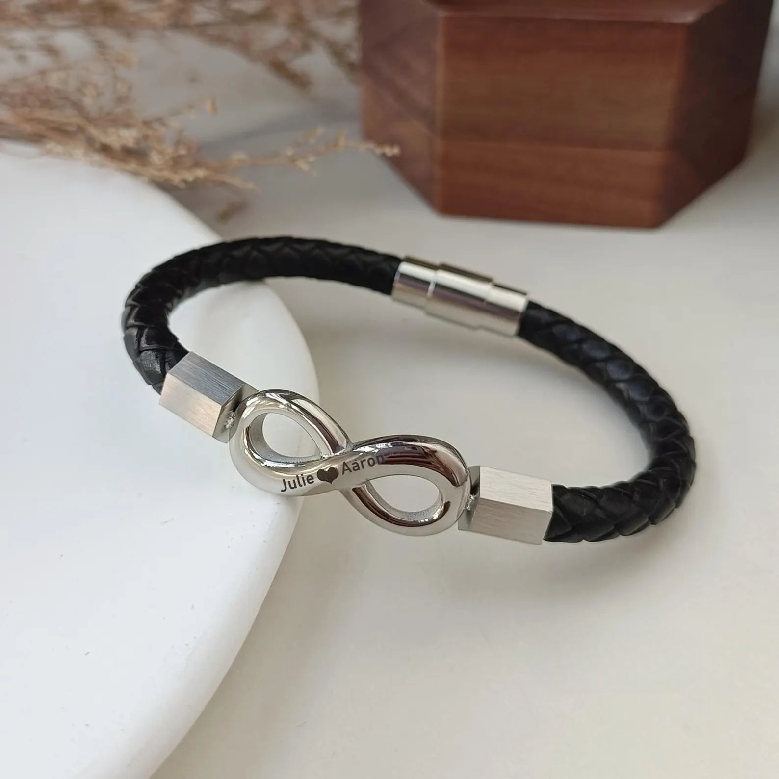Bracelet en cuir noir tressé avec ornement infini en métal argenté et fermoir magnétique assorti.