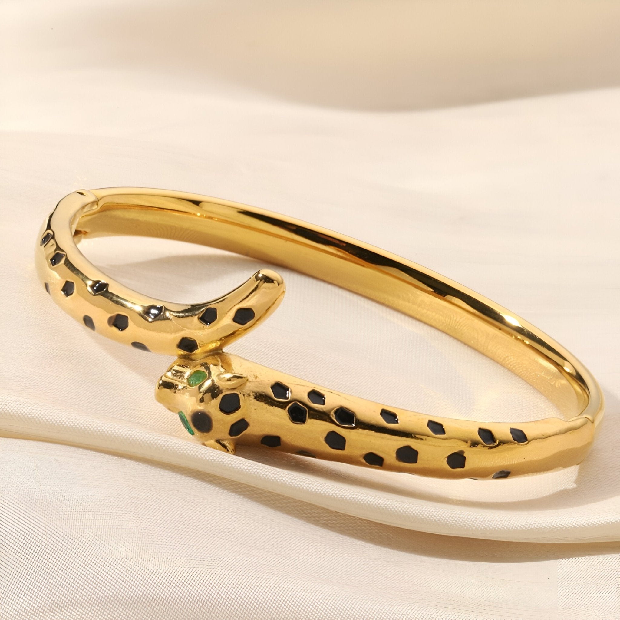 Bracelet jonc doré en forme de léopard avec taches noires et yeux verts sculptés.