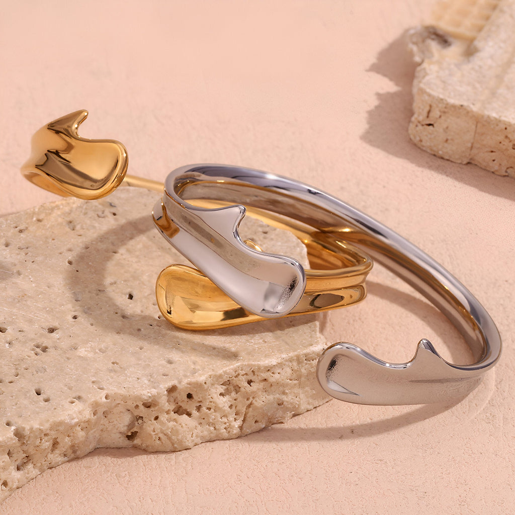 Bracelet jonc moderne ouvert en acier inoxydable argenté et doré avec extrémités arrondies design fluide.