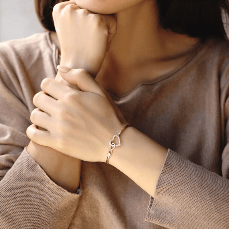 Bracelet jonc plaqué or en acier inoxydable avec pendentif cœur infini orné d'une pierre zircon claire, porté au poignet.