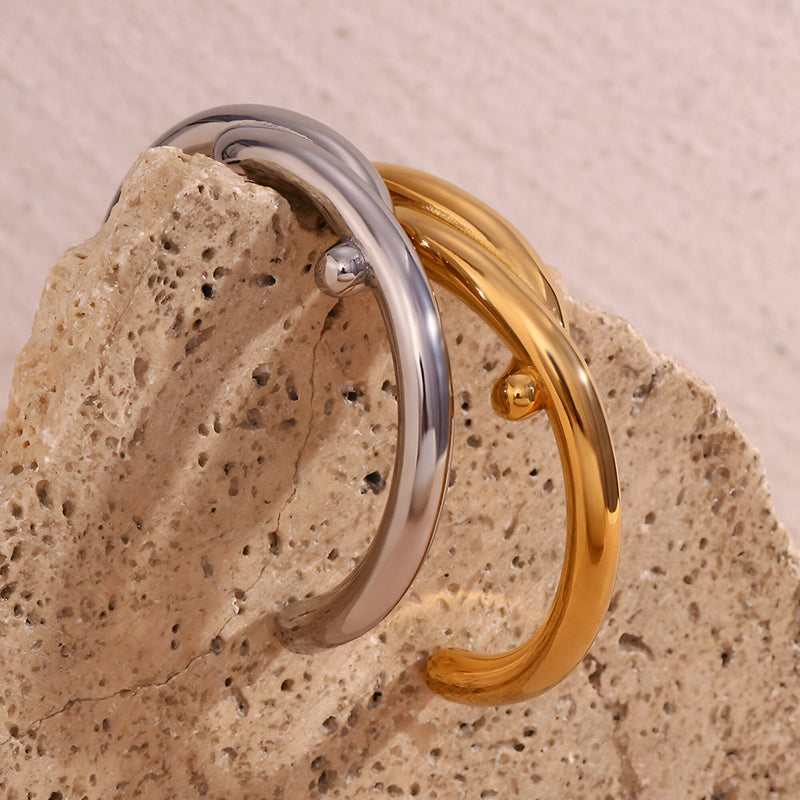 Bracelet jonc entrelacé en acier inoxydable, modèle Jovana, finition argent et or brillant sur pierre beige textured.