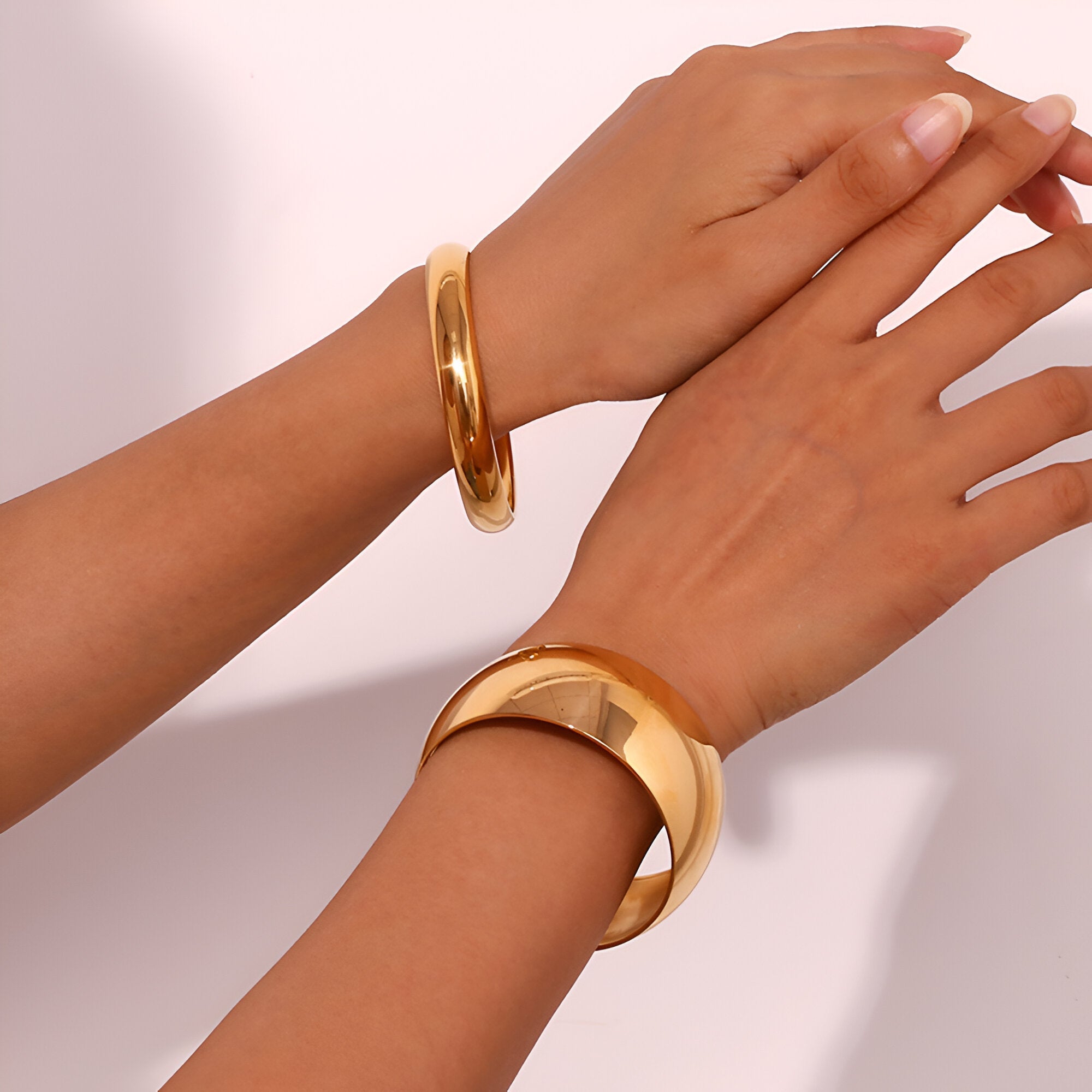 Bracelet jonc épuré en acier inoxydable doré porté aux poignets, finition lisse et brillante.