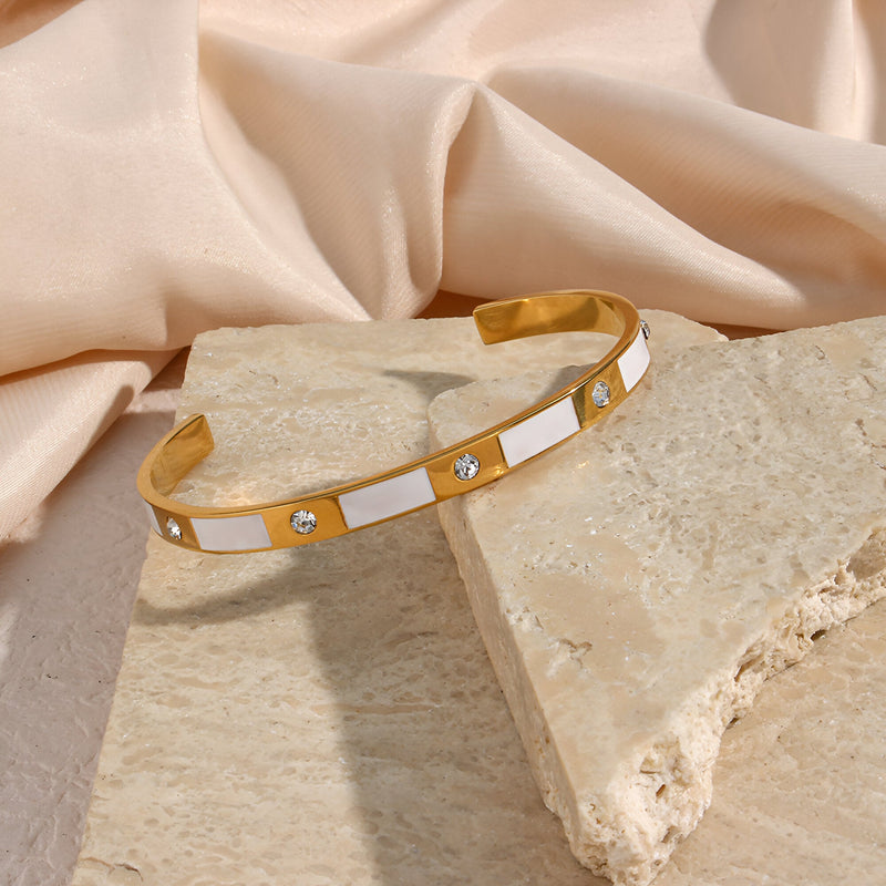 Bracelet jonc doré en acier inoxydable avec motifs géométriques blancs et incrustations de pierres brillantes.