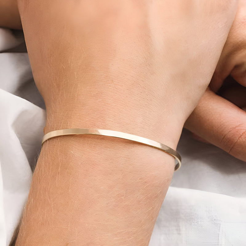 Bracelet jonc fin en acier inoxydable couleur or brillant porté au poignet féminin.