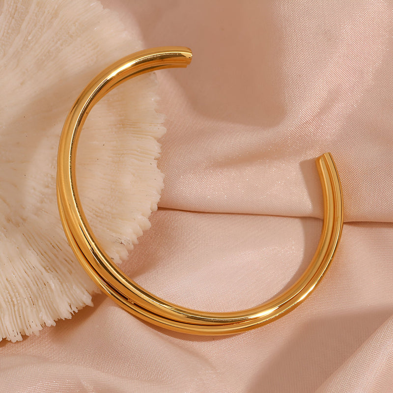 Bracelet jonc duo torsadé en acier inoxydable doré modèle Lia sur tissu rose pâle.