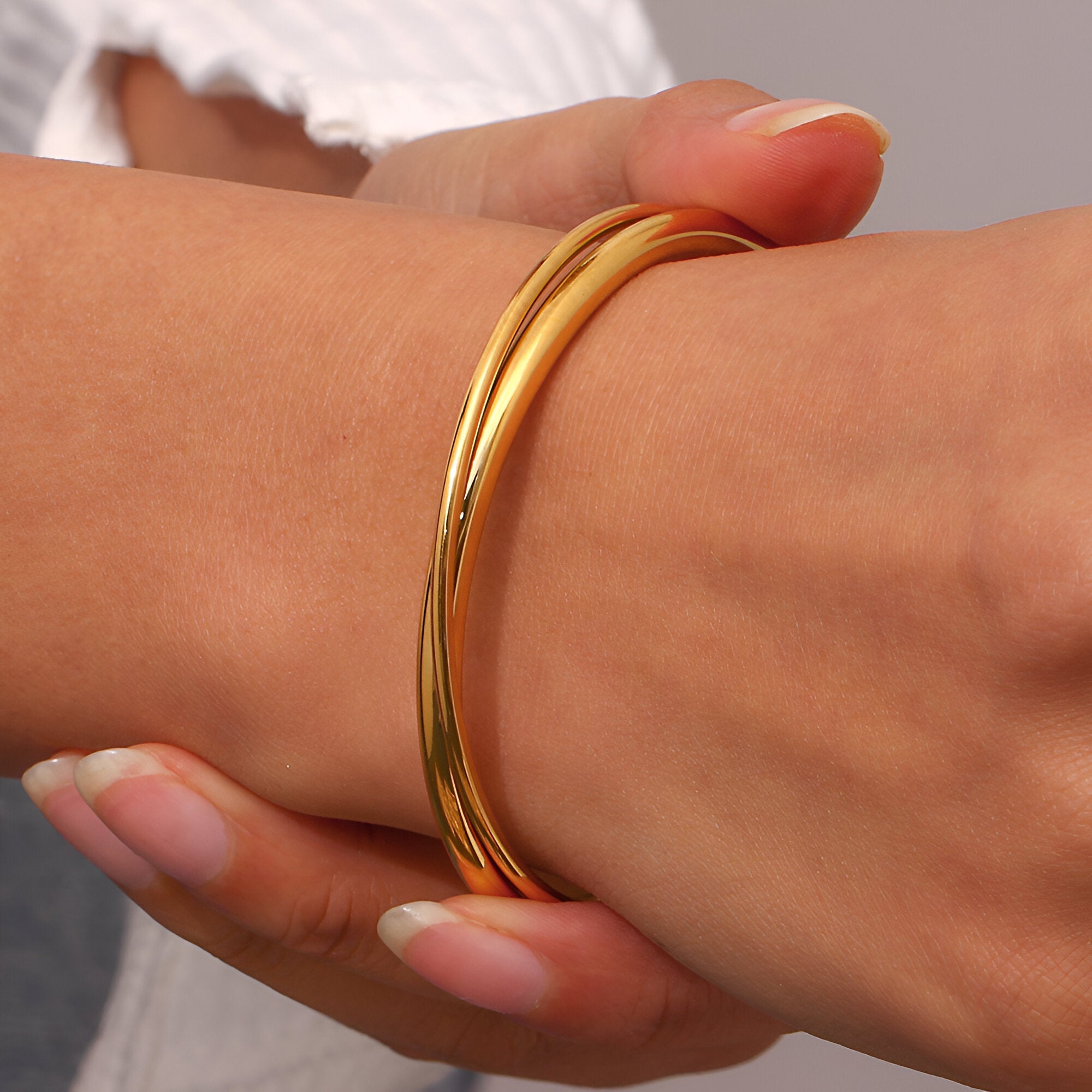 Bracelet jonc duo torsadé en acier inoxydable doré porté au poignet femme.