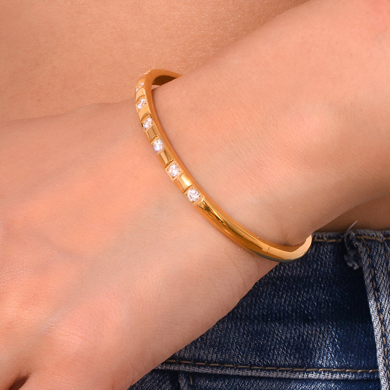 Bracelet jonc doré en acier inoxydable avec éclats rectangulaires scintillants, porté au poignet.